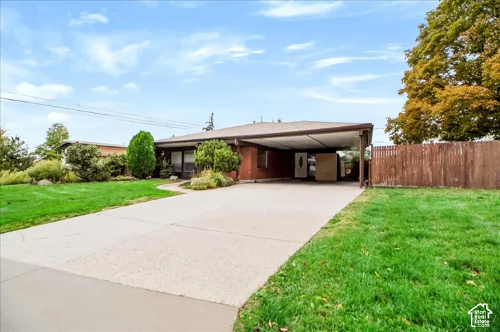 Single-story brick exterior featuring a covered carport, concrete driveway, and expansive lawn with mature landscaping
