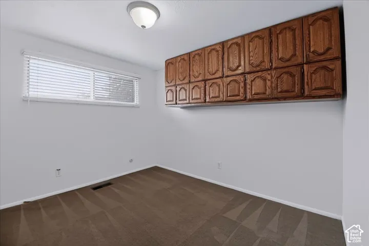 Room featuring wall-mounted wood-finish cabinetry, neutral carpeting, and a horizontal window with adjustable blinds