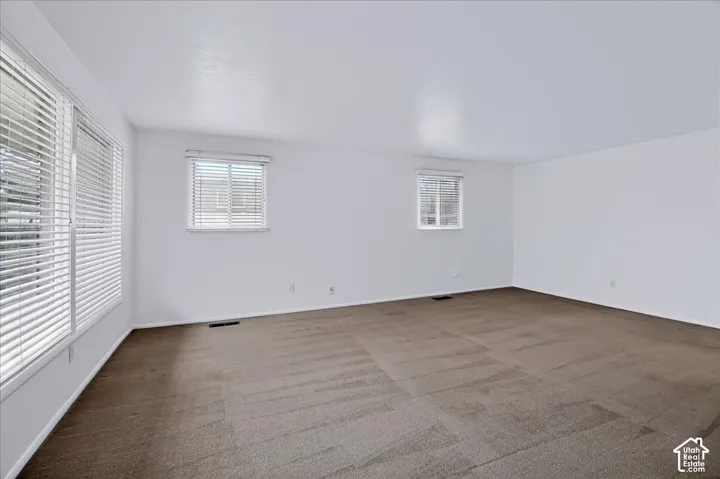 Neutral-toned wall-to-wall carpeting, multiple windows featuring adjustable horizontal blinds, and smooth-finish white walls