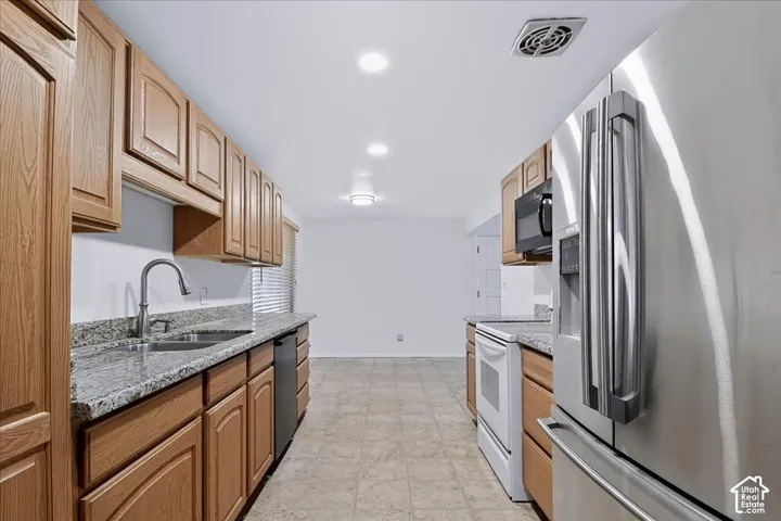 Kitchen featuring natural wood cabinetry, stone-finish countertops, stainless steel appliances, dual-basin sink, and recessed lighting