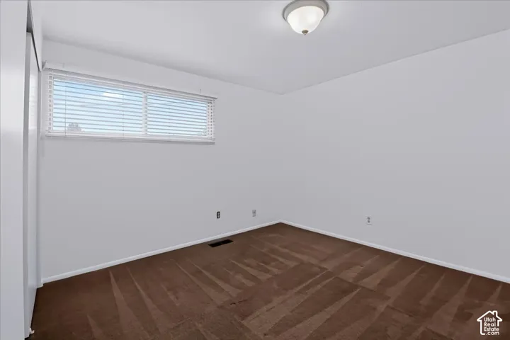 Neutral-toned interior space featuring carpeting, white wall finishes, a horizontal slider window with horizontal blinds, and a dome-style flush mount ceiling light