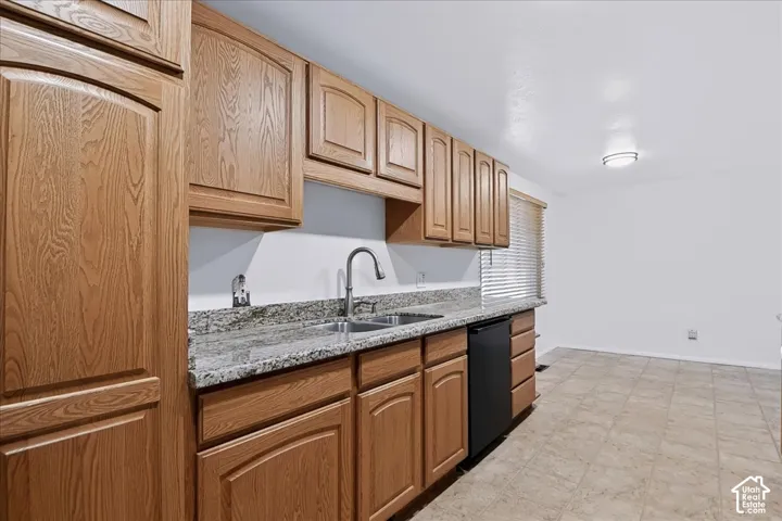 Kitchen featuring medium-tone wood cabinetry, stone-surface countertops, dual-basin stainless steel sink with high-arc faucet, black dishwasher, and ceramic tile flooring