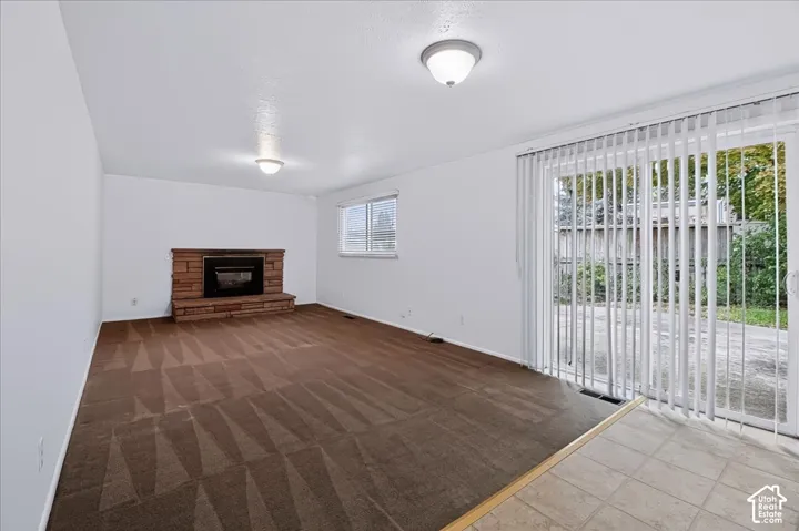 Living area featuring a masonry fireplace with a raised hearth, carpeted flooring, tile-surfaced entryway, and sliding glass doors