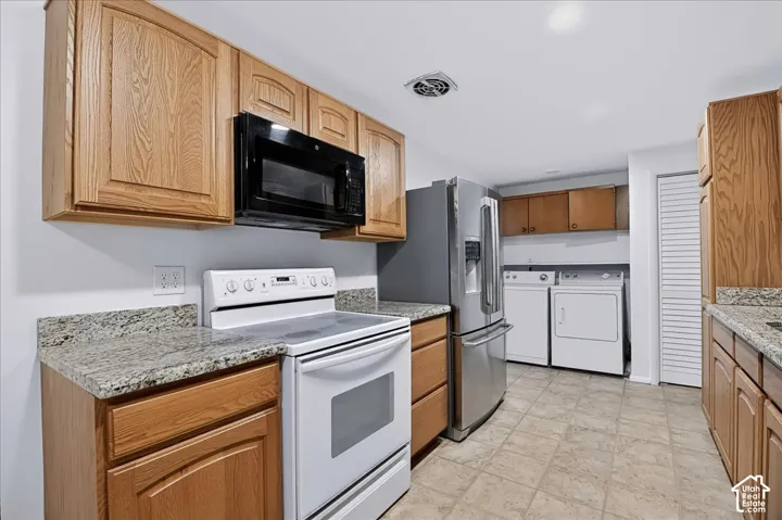 Kitchen featuring wood cabinetry, stone-finish countertops, stainless steel refrigerator, white electric range with over-the-range microwave, and tile flooring