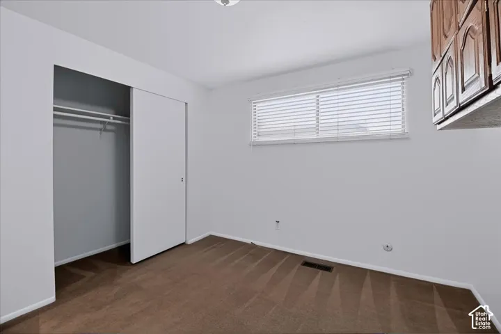 Interior space featuring wall-to-wall carpeting, a sliding-door closet, a horizontal window with slatted blinds, and mounted upper cabinetry