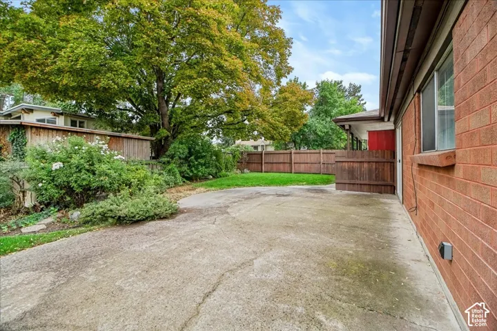Concrete patio area featuring red brick exterior siding, wood-plank fencing, and mature deciduous trees