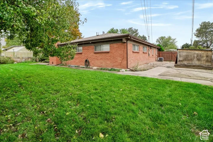 Exterior featuring a red brick facade, concrete patio, grass lawn, and wood fencing
