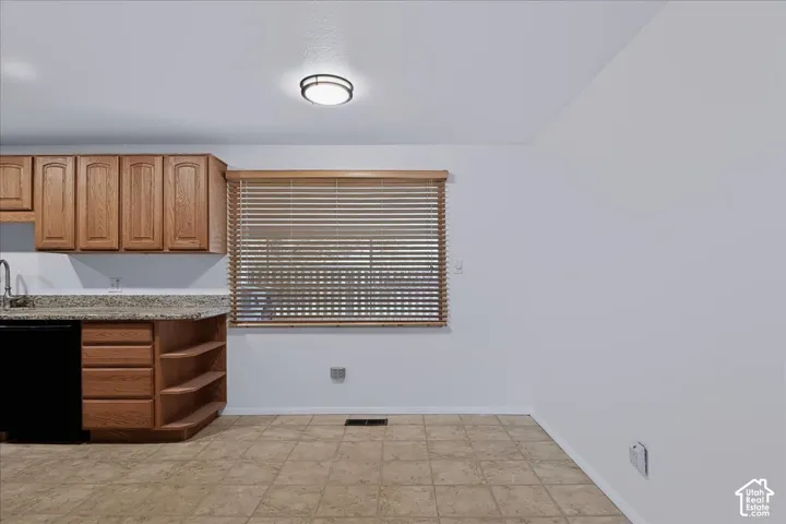 Kitchen area featuring wood cabinetry, stone-finish countertops, tiled flooring, a window with horizontal blinds, and a flush-mount ceiling light fixture