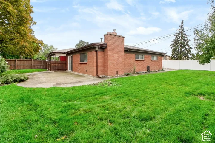 Brick exterior featuring a masonry chimney, concrete patio, wood-style privacy fencing, and expansive lawn