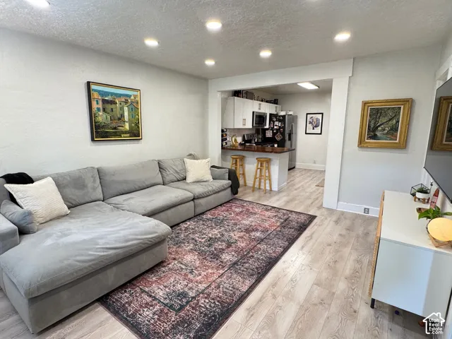 Wood-finish flooring, recessed lighting, white cabinetry, and a wooden breakfast bar