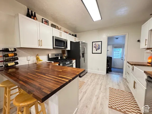 Kitchen featuring white shaker-style cabinetry, wood-finish countertops, apron-front farmhouse sink, wood-finish flooring, and subway tile backsplash
