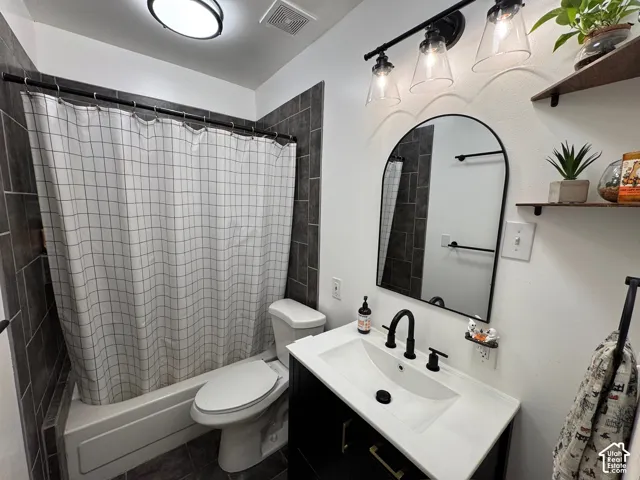 Bathroom featuring a tub-shower combination with dark charcoal tile surround, a modern vanity with a white top and undermount sink, matte black plumbing fixtures, and an arched wall mirror with a matte black frame