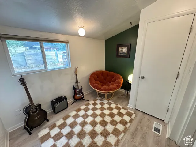 Interior room featuring wood-finish flooring, a neutral wall palette with a deep-toned accent wall, a horizontal window with roller shade, and a white interior door