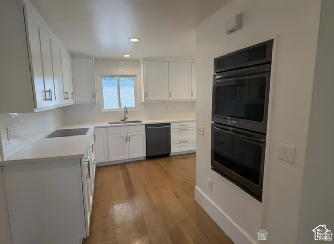 Kitchen featuring white cabinetry, wood-finish flooring, light-toned solid surface countertops, a white tile backsplash, and a built-in double oven