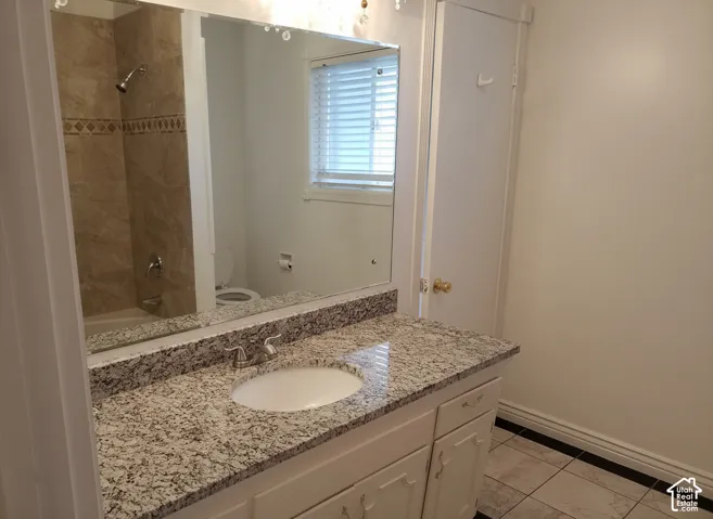 Bathroom featuring a stone-composite countertop, white vanity cabinet, large wall-mounted mirror, tile flooring, and a tub-shower combination with decorative tile inlay