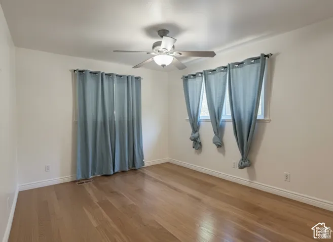 Room featuring light-toned wood-finish flooring, neutral wall paint, and a ceiling-mounted light fixture with a multi-blade fan