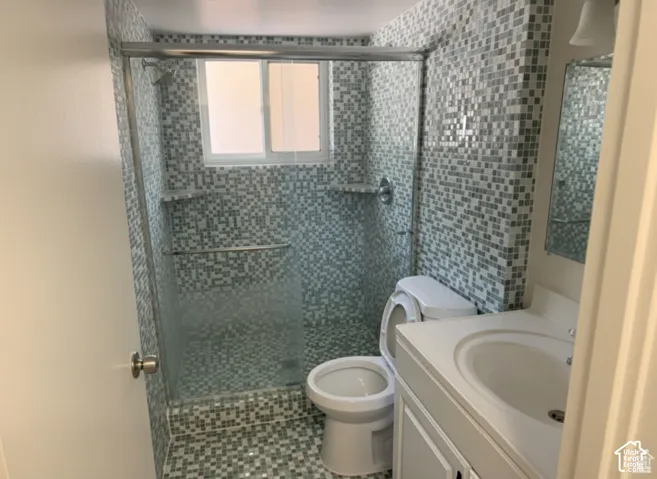 Walk-in shower enclosure with mosaic tile surround, sliding glass door, integrated stone shelving, vanity with integrated basin, and neutral-tone stone mosaic flooring