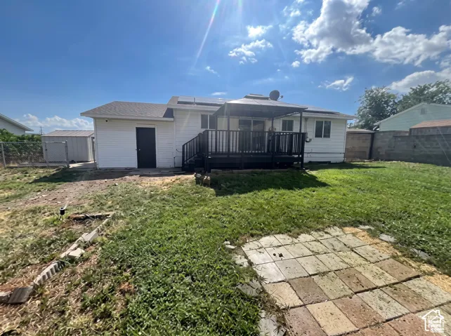 Exterior featuring white siding, a rear deck with built-in overhead canopy, solar panels, and a masonry patio