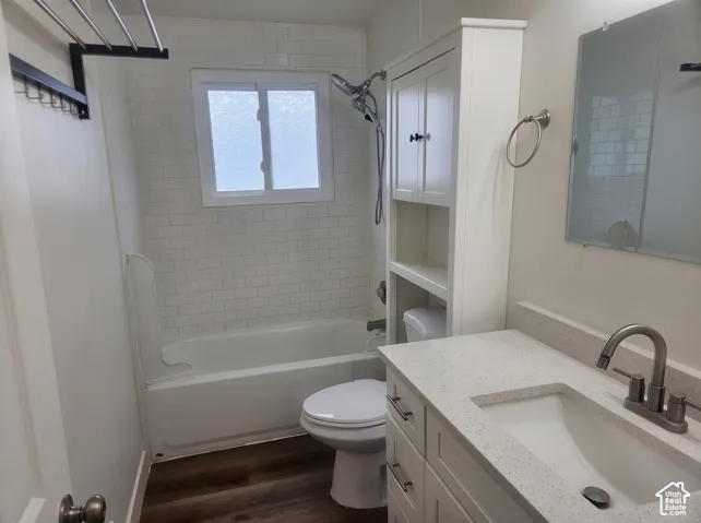 Bathroom featuring a vanity with a light-toned solid surface countertop, white cabinetry with integrated storage, wood-finish flooring, a porcelain tub with white subway tile surround, and metallic fixtures
