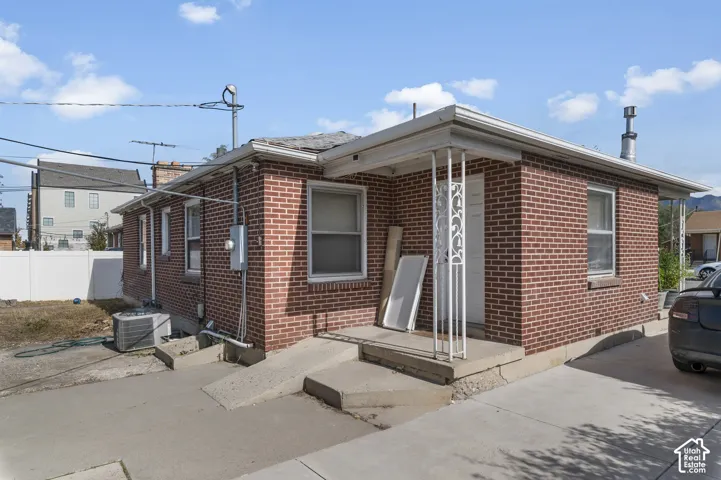 Entrance to the lower unit. Red brick exterior featuring a concrete porch with decorative metal support columns, a concrete accessibility ramp, and a vinyl fence enclosure