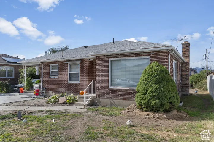 Red brick exterior featuring a shingle roof, chimney, expansive front window, and concrete entry steps with a metal railing