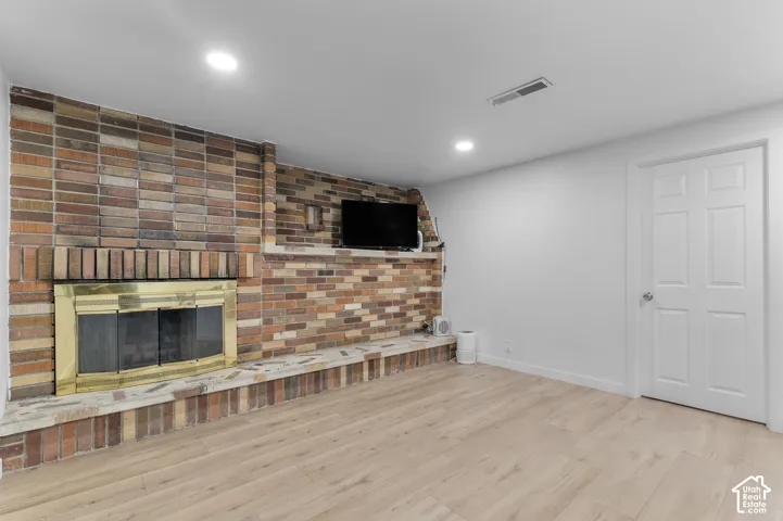 Multi-tonal brick fireplace featuring a brass-finish screen, integrated masonry hearth, wood-finish flooring, and recessed ceiling lighting