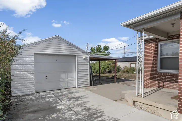 Entrance to the lower unit. Detached garage with horizontal siding, covered parking area, and concrete driveway, situated on a lot with brick-exterior structural elements