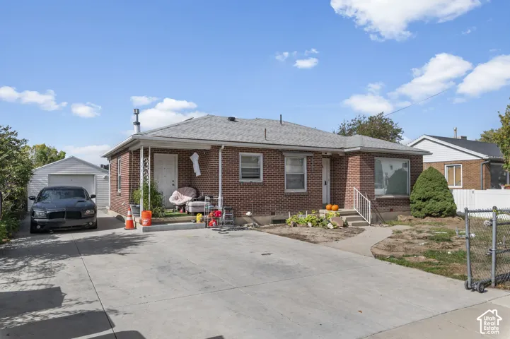 Brick exterior featuring a covered porch, concrete driveway, and detached garage