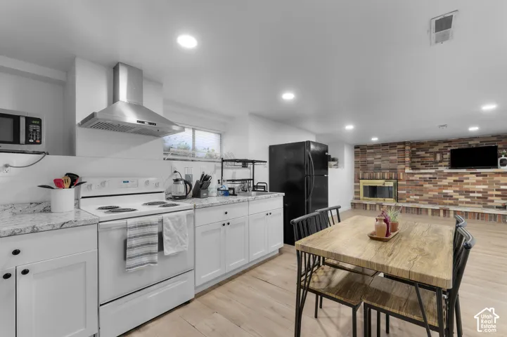 Kitchen featuring white shaker cabinetry, stone-finish countertops, stainless steel vent hood, and wood-finish flooring, complemented by a floor-to-ceiling brick fireplace