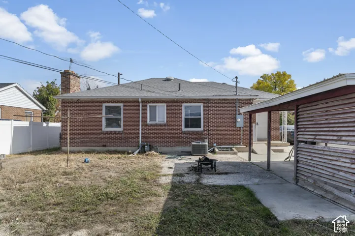 Exterior brick siding, shingle roof, masonry chimney, concrete patio, and attached covered structure