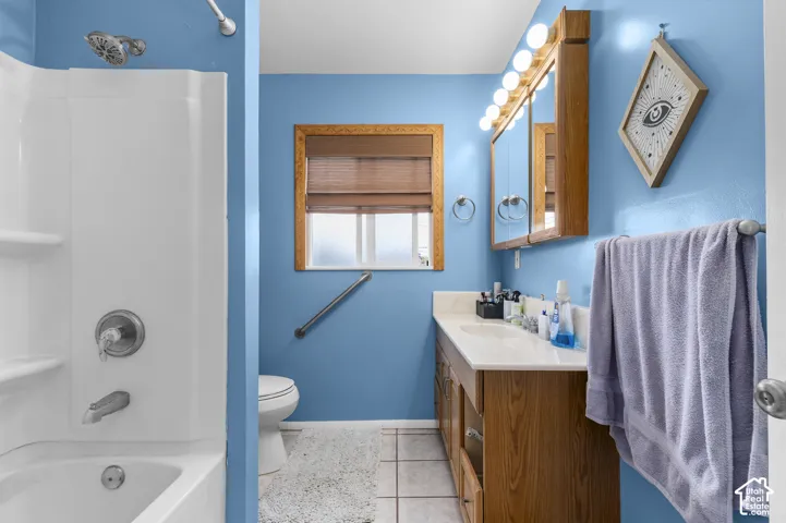 Bathroom featuring a wood-finish vanity with an integrated countertop, a multi-bulb light fixture, a composite tub and shower surround, and tile flooring