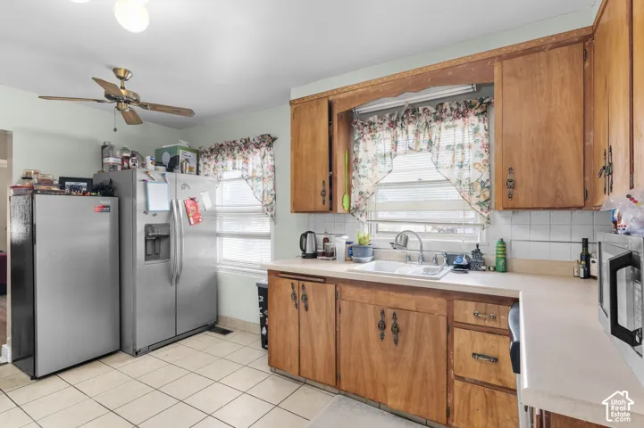 Kitchen featuring wood cabinetry, solid-surface countertops, dual-basin sink, tile backsplash, and tile flooring