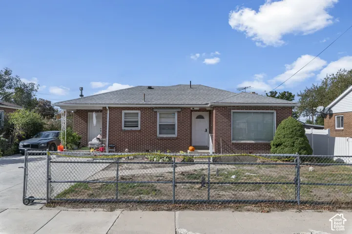 Single-story brick exterior featuring a hip roof, concrete driveway, and chain-link perimeter fencing