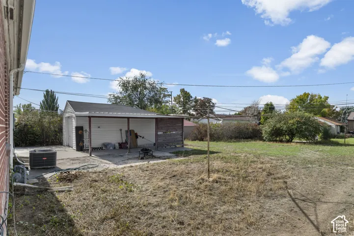Backyard featuring a detached garage with an attached carport, concrete hardscaping, and mature trees