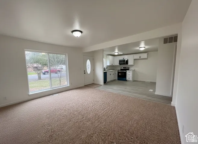 Open interior featuring wall-to-wall carpeting, wood-finish flooring, white cabinetry, a large picture window, and a door with an oval glass insert