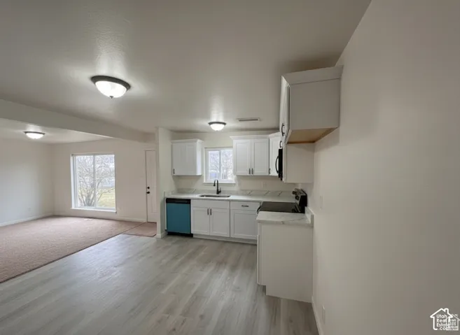 Kitchen featuring white cabinetry, light-toned countertops, a stainless steel sink with a high-arch faucet, and wood-finish flooring