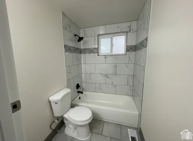 Full-size bathtub with surrounding wall tile, decorative mosaic tile inlay, matte black shower fixtures, and large-format floor tile