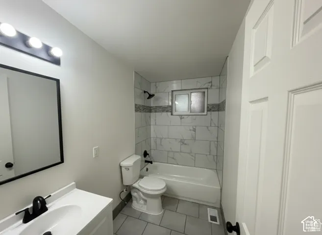Bathroom featuring a tub with floor-to-ceiling subway tile surround, mosaic tile accent, vanity with matte black faucet, and rectangular mirror with matching frame