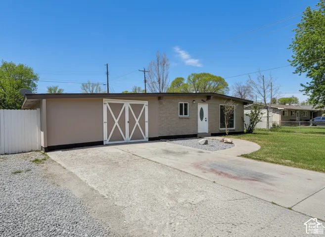 Single-level exterior featuring a brick facade, attached garage with carriage-style doors, concrete driveway, and white vinyl privacy fencing