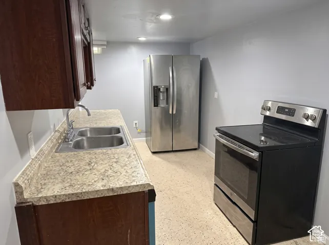 Kitchen featuring rich-toned cabinetry, stone-patterned laminate countertops, a double-basin stainless steel sink, a stainless steel side-by-side refrigerator, and a black electric range