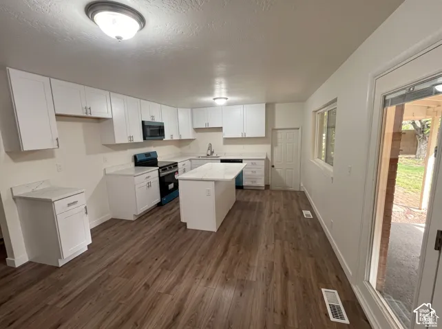 Kitchen featuring white shaker-style cabinetry, stone-finish countertops, a central island, wood-finish flooring, and built-in microwave
