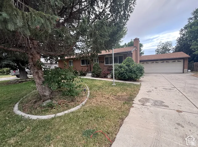 Single-story brick exterior featuring a multi-car attached garage, asphalt shingle roof, concrete driveway, and mature coniferous landscaping
