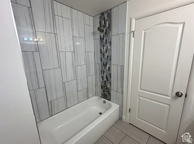 Bathtub area featuring large-format linear wall tile, a vertical mosaic accent strip, brushed metal fixtures, and ceramic floor tiling
