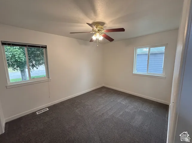 Room featuring wall-to-wall carpeting, dual windows, and a ceiling fan with integrated light fixture