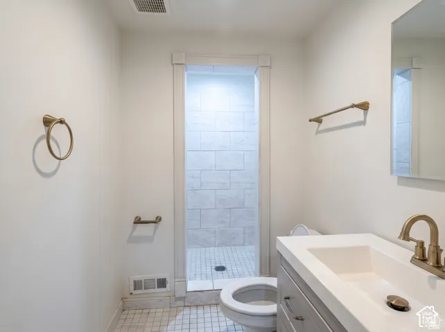 Bathroom featuring a vanity with integrated sink, brass-tone hardware, a tiled walk-in shower with stone-patterned wall surfacing, and a frameless mirror