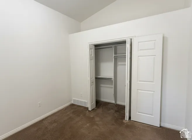 Vaulted ceiling, neutral carpet flooring, and closet featuring built-in shelving and hanging rods