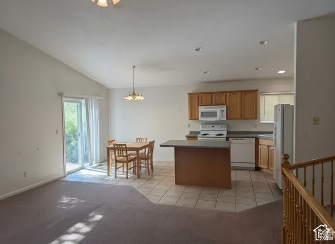 Vaulted ceiling, kitchen island, wood-finish cabinetry, tile flooring, and sliding glass door