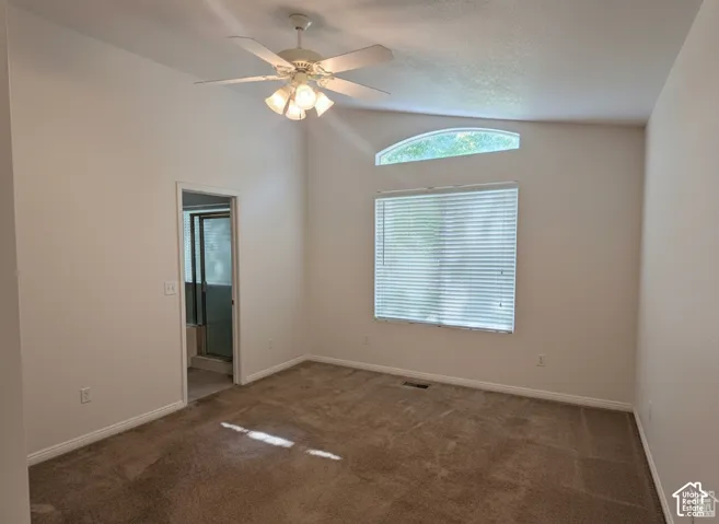 Vaulted ceiling, arched transom window, white-finish ceiling fan with integrated lighting, and neutral carpeting