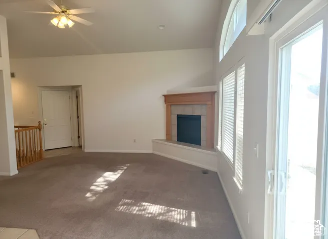 Vaulted ceilings, corner fireplace with wood mantle and tile surround, arched transom window, sliding glass door, and wooden staircase railing