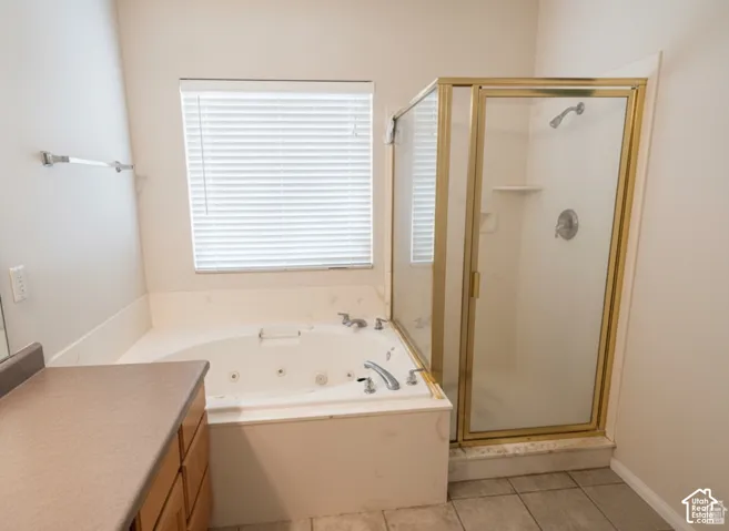 Jetted soaking tub, separate glass-enclosed shower with gold-tone frame, neutral-toned solid surface vanity countertop, and ceramic tile flooring